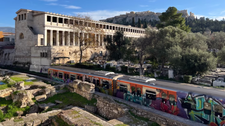 The Ancient Agora of Athens archaeological site is to the north of the Acropolis Hill. The entrance is via a bridge across the railway line that cuts through parts of the site.